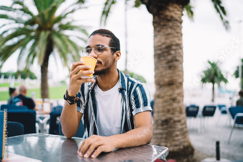 Fotografia Young ethnic male drinking coffee in outdoor cafe