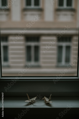 Handmade paper origamis representing similar cranes against window and house facade in twilight on blurred background photo