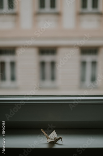 Handmade paper origami representing similar cranes against window and house facade in twilight on blurred background photo