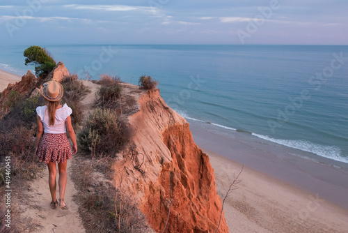 Back view of unrecognizable woman standing in mountain cliff in the coastline during beautiful sunset in Tavira in Algarve, Portugal photo