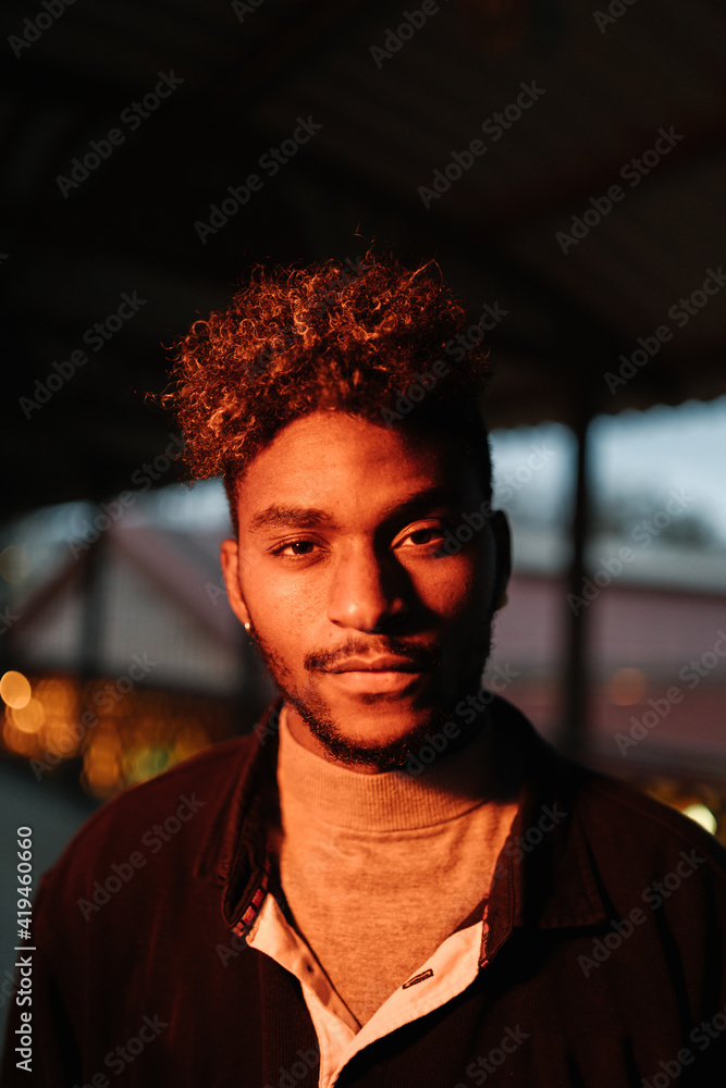Young African American hipster male with curly hair and beard wearing warm jacket looking at camera while standing against shabby wall Young African American hipster male with curly hair and beard wearing warm jacket looking at camera while standing against shabby wall