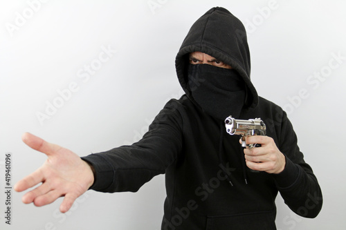 Criminal man wearing black mask and hoodie pointing a gun while asking for money. Crime concept