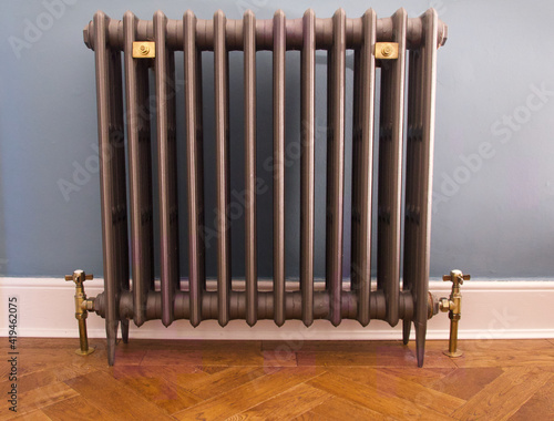 Old fashioned cast iron radiator with brass fittings on herringbone wooden floor