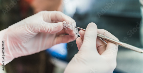 Crop unrecognizable dentist in latex gloves holding ultra thin veneers and scaler while working in dental clinic photo