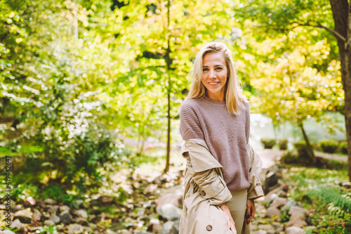 Caucasian blonde woman wearind trench smile happily on sunny spring day outside walking in park. photo