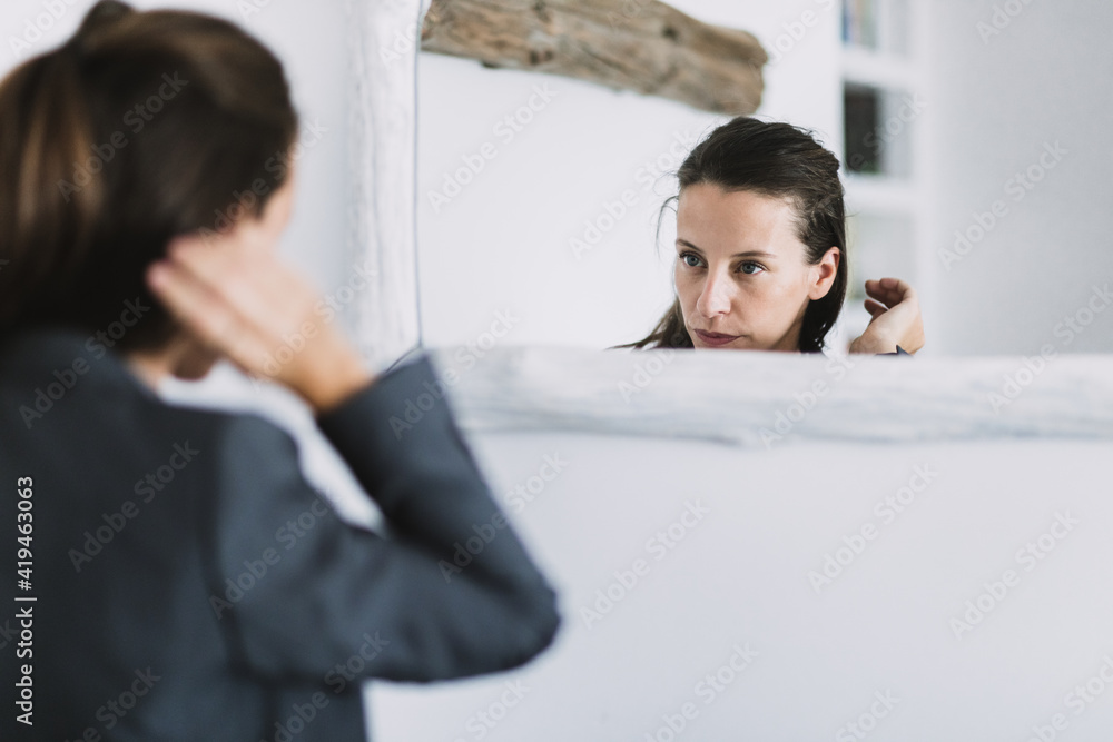 Young female in formal outfit looking at mirror and adjusting hair while preparing for workday in morning Young female in formal outfit looking at mirror and adjusting hair while preparing for workday in morning
