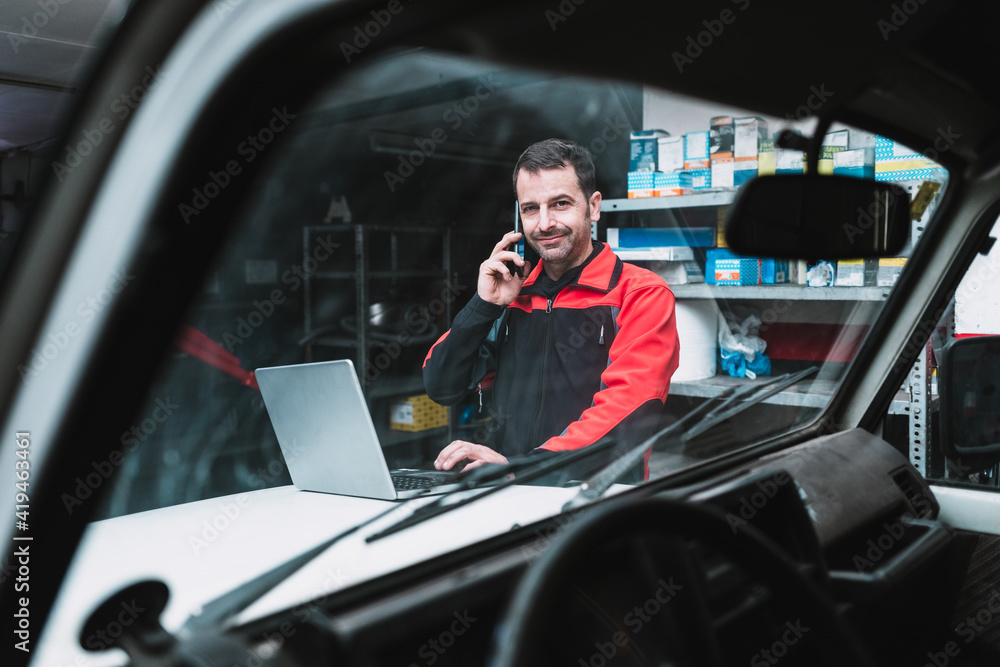 Male master with netbook talking on cellphone near transport in garage Male master with netbook talking on cellphone near transport in garage
