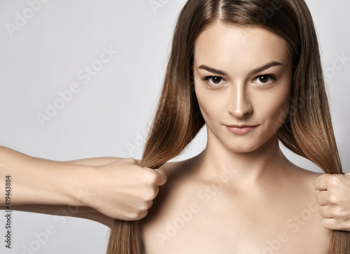 Portrait of young beautiful woman with silky long straight hair looking at camera and holding her strong healthy hair in hands over grey background. Hairstyle, hairsalon, hairdresser, fashion concept