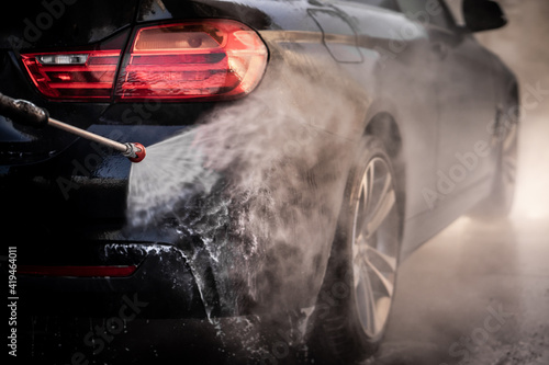 A man washes his luxury black sports car in a manual car wash.