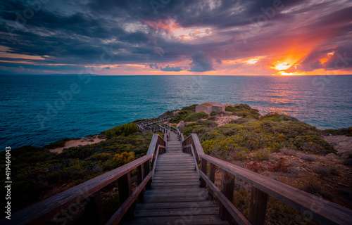 Wonderful scenery of endless wooden stairs leading to calm sea under colorful cloudy sky at sunset in Cadiz