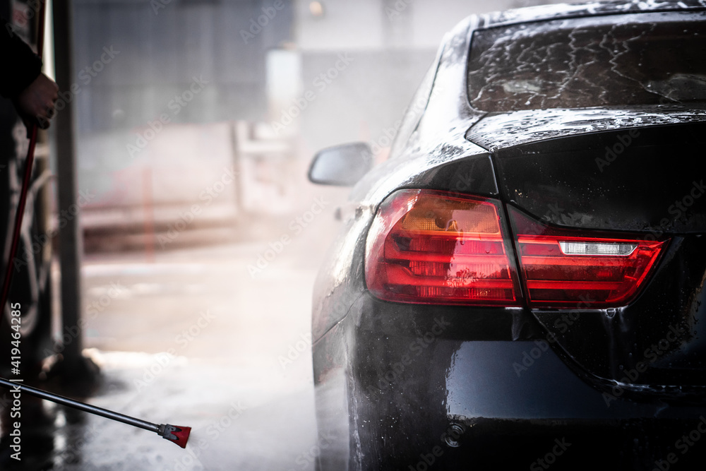 A man washes his luxury black sports car in a manual car wash.