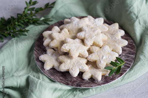 Sable sugar cookies with sugar powder on a plate on gteen napkin, green leavs in background. Selective focus