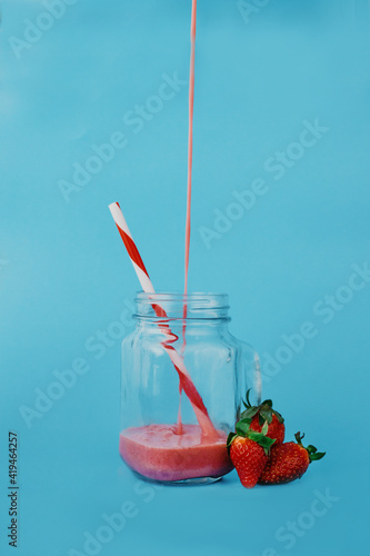 Glass jar with flow of tasty beverage with striped drinking tube near whole strawberries photo