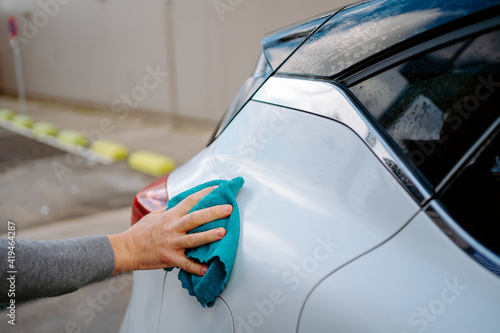 Cropped unrecognizable young male wiping vehicle with rag while standing in car wash station against cloudy sky photo