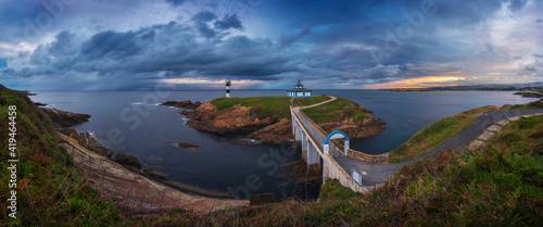 Scenic view of small island with lighthouse called Faro de Cabo Mayor connected with coastline by bridge under dramatic cloudy sky at sunset time in Santander in Spain photo