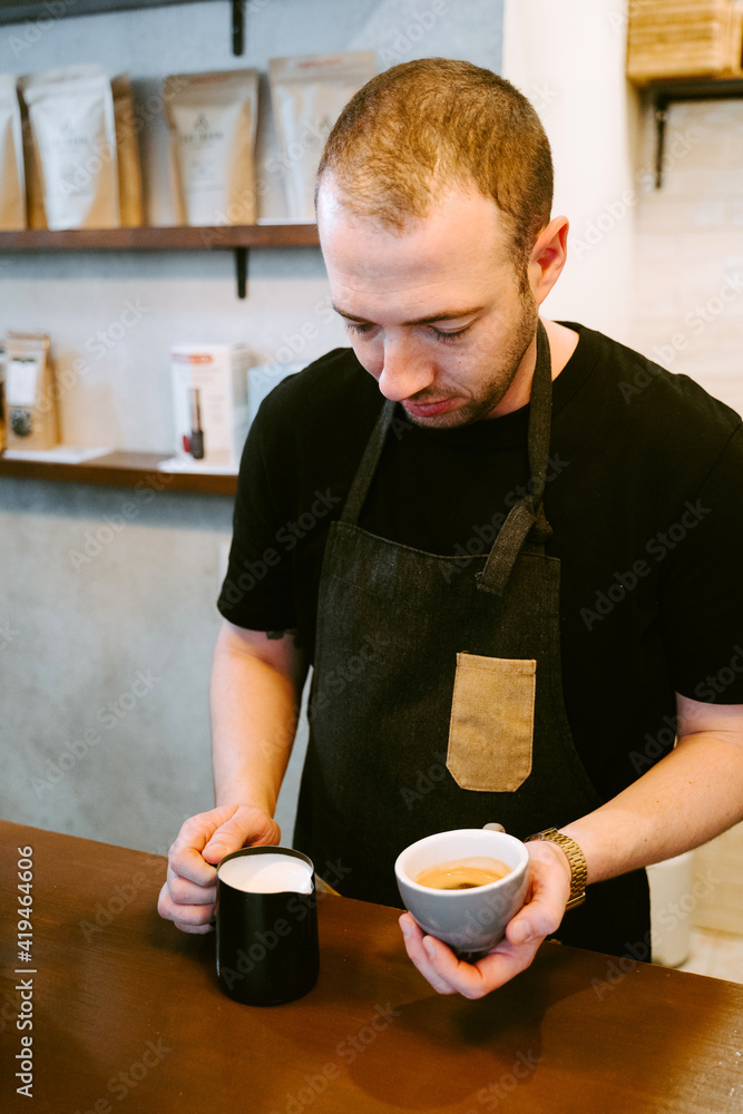 Close-up of a waiter serving milk to a cup of coffee Close-up of a waiter serving milk to a cup of coffee