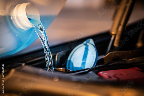 Pouring blue antifreeze liquid for washing car screen.