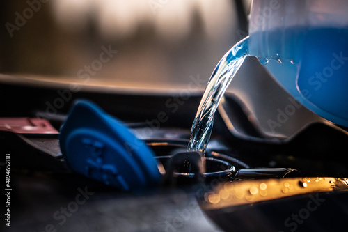 Pouring blue antifreeze liquid for washing car screen.
