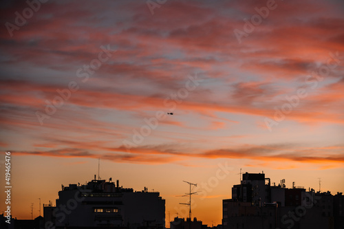 Remote view of helicopter silhouette on background of vivid sundown sky over city in evening