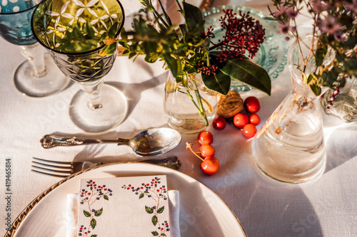 High angle of served festive table with crystal glasses cutlery napkin on plate near bunch of fresh flowers for wedding and menu card photo