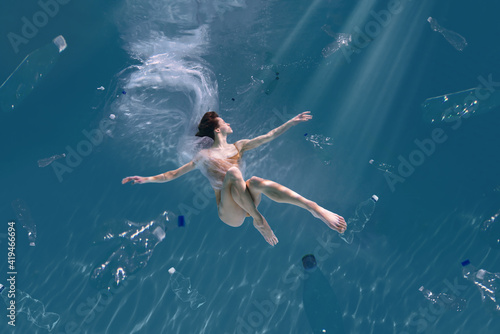 Fashionable and athletic girl free diver alone in the depths of the ocean. Swimmer brunette diving deep in ocean on blue underwater background. Pollution, plastic and ecology concept © Monstar Studio