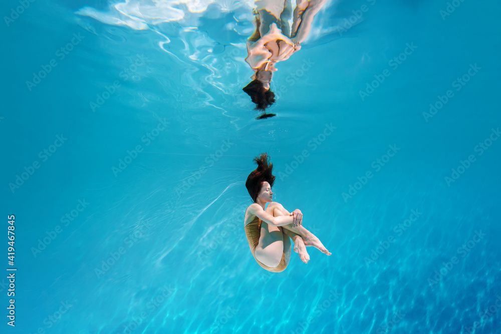 Fashionable and athletic girl free diver alone in the depths of the ocean. Swimmer brunette diving deep in ocean on blue underwater background. Concentration, freedom and beauty concept
