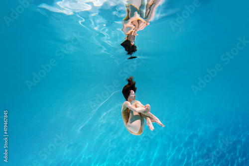 Fashionable and athletic girl free diver alone in the depths of the ocean. Swimmer brunette diving deep in ocean on blue underwater background. Concentration, freedom and beauty concept © Monstar Studio