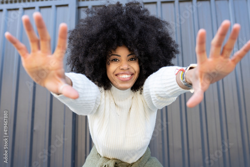 Cheerful young African American lady with curly hair in casual clothes showing two hands and looking at camera on street photo