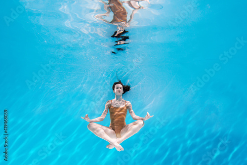 Fashionable and athletic girl free diver alone in the depths of the ocean. Swimmer brunette diving deep in ocean on blue underwater background. Concentration, freedom and beauty concept