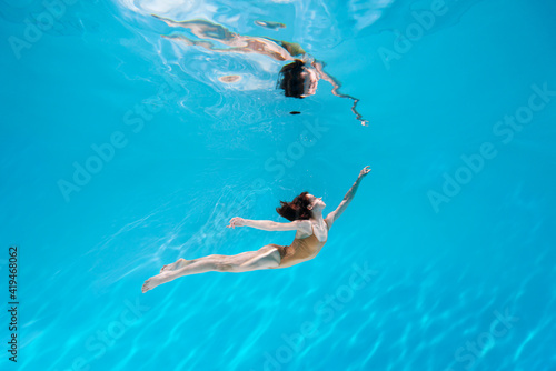 Fashionable and athletic girl free diver alone in the depths of the ocean. Swimmer brunette diving deep in ocean on blue underwater background. Concentration, freedom and beauty concept © Monstar Studio
