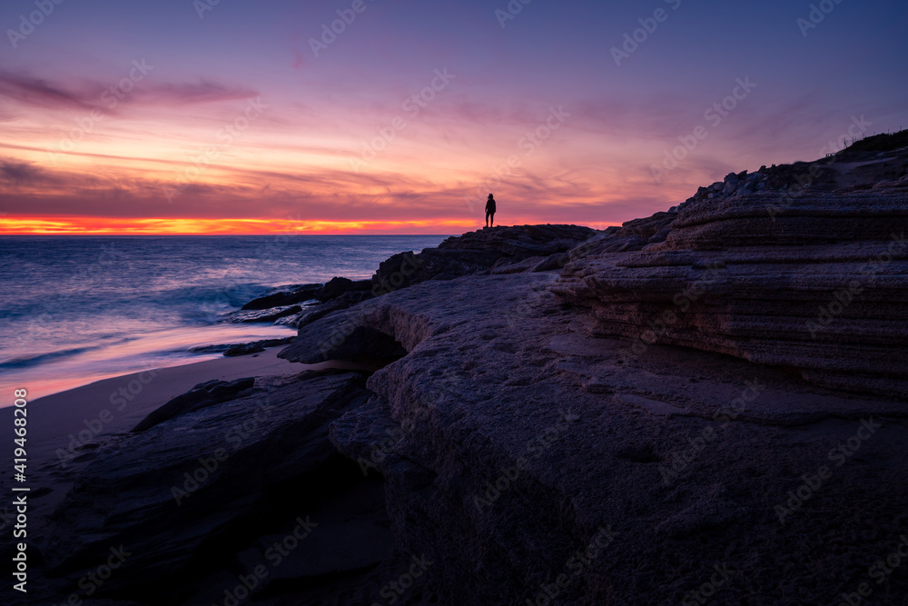 Silhouette of faceless tourist standing on rock and admiring breathtaking scenery of vibrant sunset sky over sea in Cadiz Silhouette of faceless tourist standing on rock and admiring breathtaking scenery of vibrant sunset sky over sea in Cadiz
