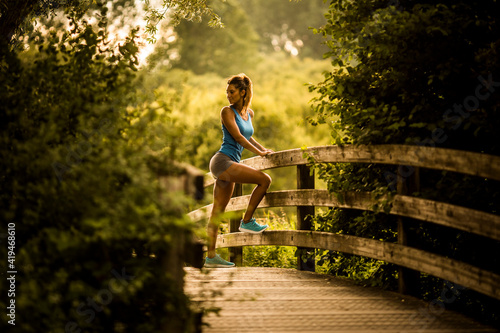 Determined slim sportswoman stretching legs during workout in summer in Salburua park photo