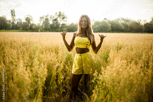 Cheerful young female in yellow summer wear showing shaka sign while standing in field in Salburua park and looking at camera photo