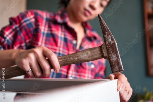 From below focused ethnic female using hammer for nailing wooden dowels while assembling new furniture in apartment photo