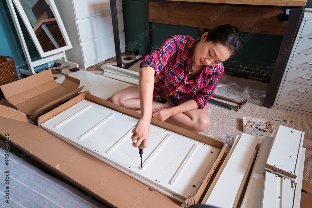 © Juan Alberto Ruiz/ADDICTIVE STOCK - From above ethnic Asian female sitting on floor and screwing screws in wooden board while assembling new furniture at home © Juan Alberto Ruiz/ADDICTIVE STOCK - From above ethnic Asian female sitting on floor and screwing screws in wooden board while assembling new furniture at home