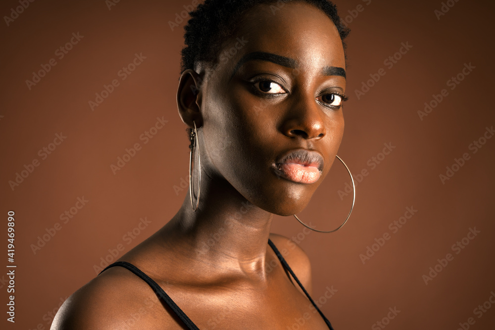 Slender black woman with short hair standing against brown background ...