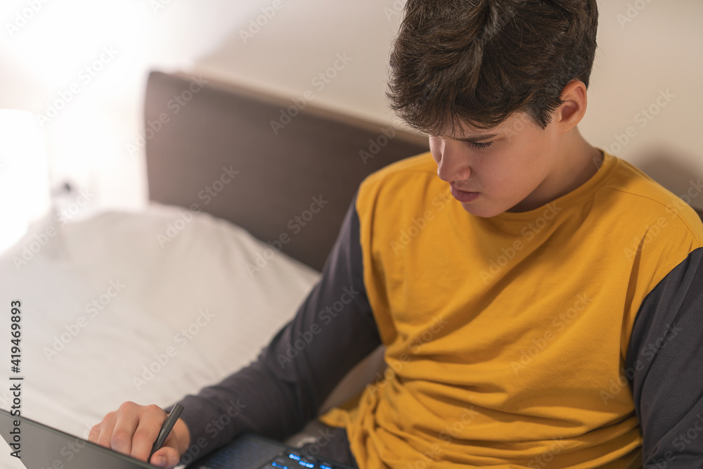 
Young man is sitting in the bed and working on a laptop computer