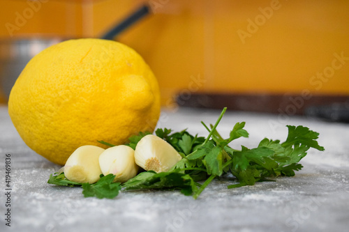 Close up view of yellow lemon with garlic and parsley in a blurred background