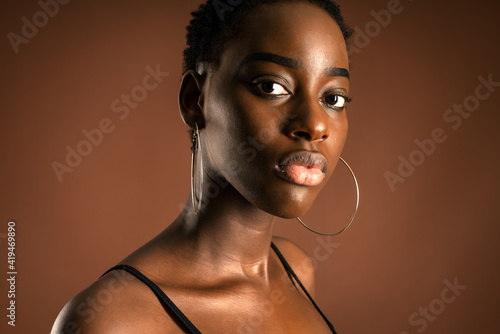 Slender black woman with short hair standing against brown background looking at camera photo