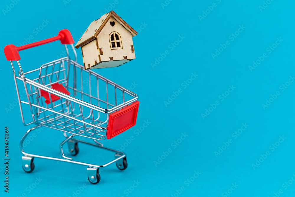 Buying a house or mortgage concept. Model toy house flying with shopping cart on blue background. Housing and Real Estate concept.