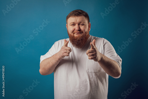 portrait of a bearded cheerful, emotional and interesting man in a white T-shirt on a blue background, showing various hand gestures. Cheerful guy show business artist, host of a glamorous show. Body 
