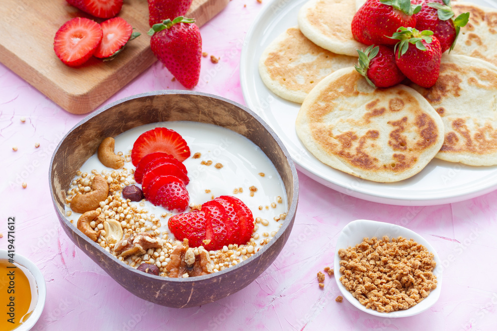 Top view of table with bowl of granola and yoghurt and homemade pancakes with strawberries served for delicious breakfast in morning Top view of table with bowl of granola and yoghurt and homemade pancakes with strawberries served for delicious breakfast in morning