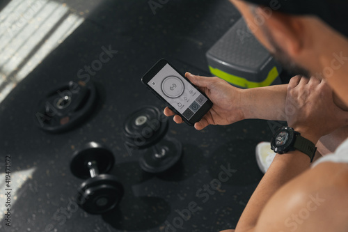 A man with a smart phone in the gym. Looking at the screen of the smart phone. With dumbbells on the floor. health and wellness concept.