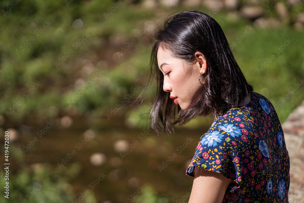 Side view of tranquil Asian female standing in nature in Taiwan on sunny day in summer and looking down Side view of tranquil Asian female standing in nature in Taiwan on sunny day in summer and looking down