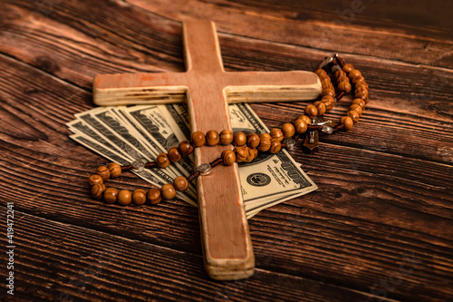 Photography A Catholic cross, a rosary with beads and dollars lie on a dark brown wooden table
