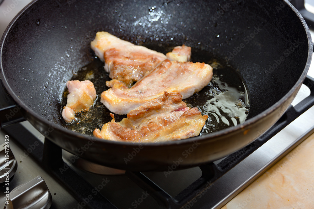 Chunks of raw meat are fried in sunflower oil on a hot stove at home in the kitchen.