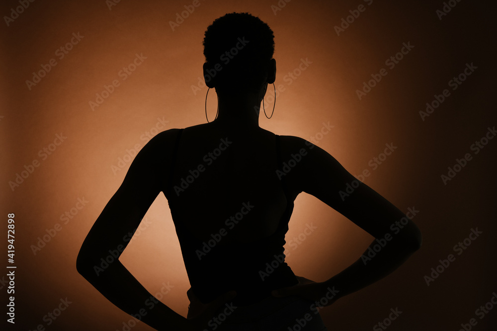 Silhouette of unrecognizable slender female with hands on wait against brown background Silhouette of unrecognizable slender female with hands on wait against brown background