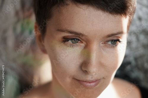 Crop feminine thoughtful adult lady with natural makeup and short hair smiling and looking away dreamily in sunlight