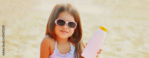 Summer vacation, portrait little girl child showing sunscreen skin bottle on beach