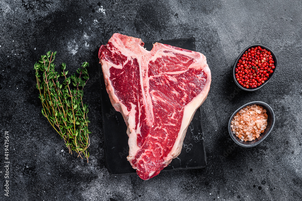 Dry-aged Raw T-bone or porterhouse beef meat Steak with herbs and salt. Black background. Top view